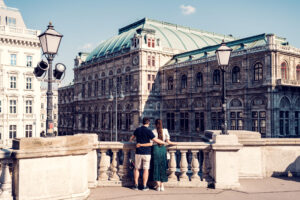 Adriana and Mario on the sunny Albertina terrace, looking across the stone balustrade at the State Opera.
