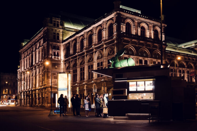 Long line of people in front of Bitzinger Würstelstand, with the historic State Opera in the background.