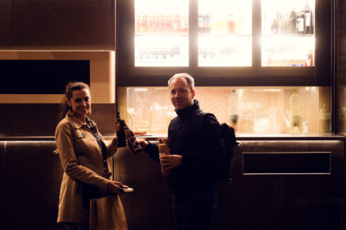 Adriana and Mario cheering with beer in front of Bitzinger Würstelstand, celebrating the vibrant atmosphere of Vienna.