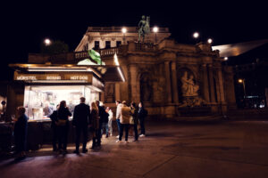 Visitors queuing at Bitzinger Würstelstand, with the iconic Albertina providing a stunning backdrop.