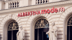 Close-up of the Albertina Modern red lettering between classical statues and arched windows.