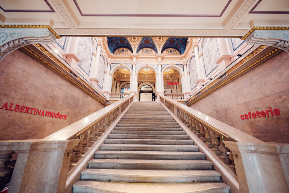 The grand staircase at Albertina Modern museum, with marble steps leading up to elegant arches and a richly decorated ceiling.