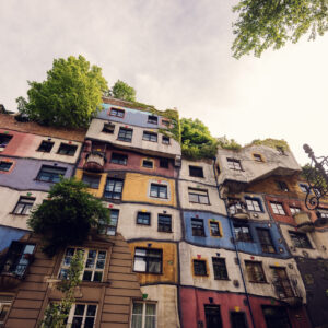 Bunte Fenster des Hundertwasserhauses, jedes mit einer anderen Form und Rahmung.