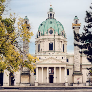 Die Karlskirche in Wien, eine Barockkirche mit einer großen grünen Kuppel und zwei verzierten Säulen zu beiden Seiten des Eingangs.