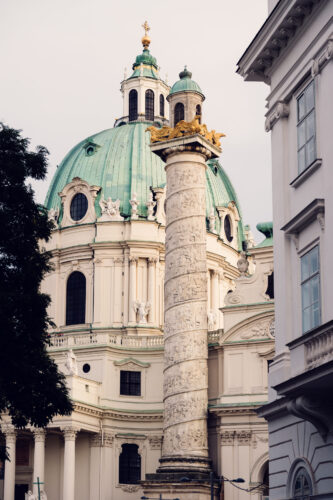 Vista lateral de la Karlskirche en Viena, destacando una de las columnas talladas y la cúpula verde.