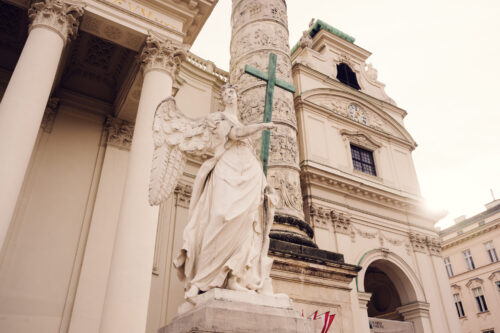 A close-up of a statue of an angel positioned in front of one of the ornate columns.
