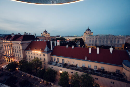Evening view from the MQ Libelle terrace over the illuminated MuseumsQuartier buildings.