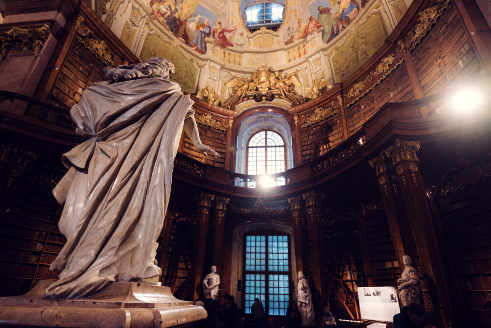 Golden afternoon light filtering through the Prunksaal's tall windows, creating magical atmosphere for photography.