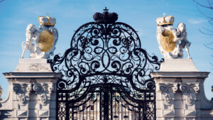 Puerta de entrada de El Belvedere bañada por el sol, con esculturas y forja bajo un cielo azul intenso.