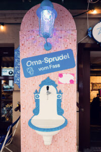A drinking fountain at Vollpension labeled "Oma-Sprudel vom Fass" ("Grandma’s sparkling water from the tap").