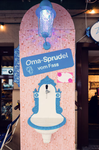 A drinking fountain at Vollpension labeled "Oma-Sprudel vom Fass" ("Grandma’s sparkling water from the tap").