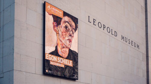 Exterior of Leopold Museum Vienna with its distinctive white limestone cube design in the MuseumsQuartier, housing the world's largest Egon Schiele collection with promotional banners featuring his iconic expressionist artwork visible on the minimalist facade.
