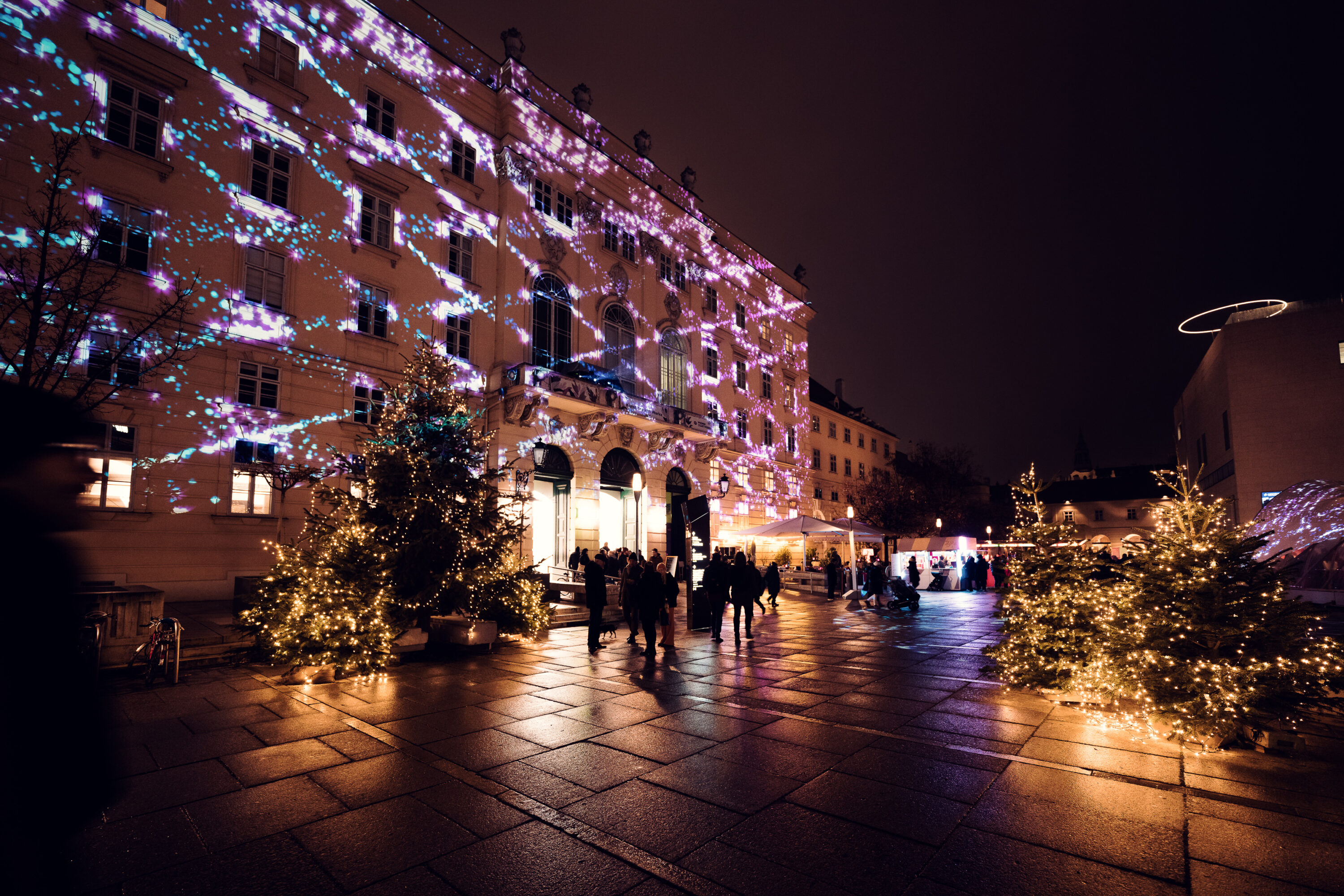 Evening atmosphere in MQ main courtyard with illuminated cultural institutions and social gatherings.