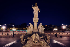 Fuente de Palas Atenea iluminada de noche frente al Parlamento austriaco con un tranvía al fondo.