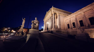 Estatua de Palas Atenea y escultura sentada frente al Parlamento austriaco iluminado de noche.