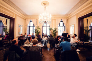 Clients attablés dans le salon principal du Café Demel avec lustre en cristal et grandes fenêtres.