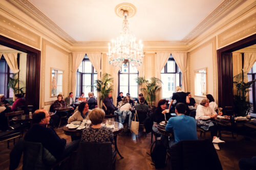 Clients attablés dans le salon principal du Café Demel avec lustre en cristal et grandes fenêtres.