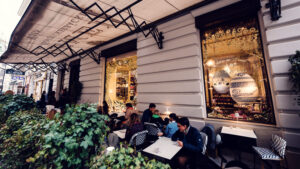 Terrasse du Café Demel sur le Kohlmarkt avec des clients et vue sur la vitrine dorée.