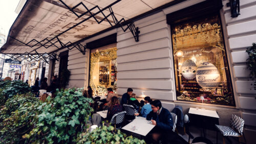 Terrasse du Café Demel sur le Kohlmarkt avec des clients et vue sur la vitrine dorée.
