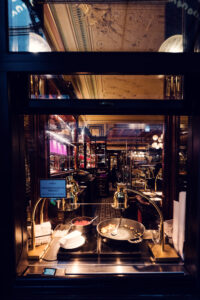 Vue à travers la vitre sur la cuisine ouverte du Café Demel avec poêles et ingrédients.