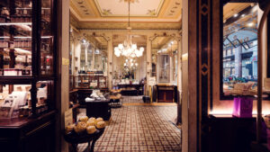 Vue depuis l'entrée du Café Demel avec lustre en cristal, sol en mosaïque et vitrines de pâtisseries.