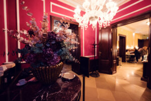 Salon rouge du Café Demel avec arrangement floral, lustre en verre et portes en bois sombre.