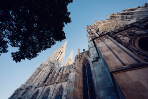 Votivkirche Vienna's distinctive limestone exterior with intricate tracery windows and Gothic details against deep blue summer sky.