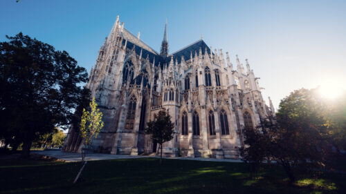 Side view of the Votivkirche (Votive Church) Vienna showing flying buttresses and detailed stonework with lush summer greenery surrounding the base.