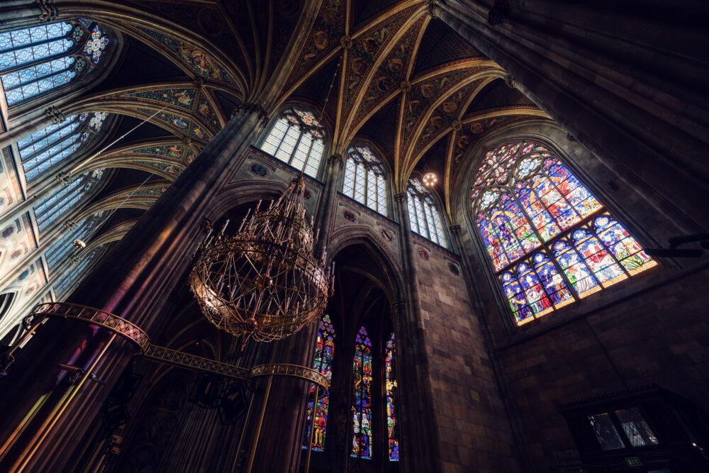 Dramatic perspective of Votivkirche Vienna's architectural masterpiece with soaring vertical lines, perfectly balanced proportions, and the play of light through stained glass windows illuminating the limestone surfaces of this 19th century neo-Gothic marvel.