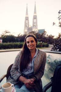 Adriana enjoying a traditional Wiener Melange coffee with the impressive neo-Gothic twin spires of Votivkirche Vienna (Votive Church) rising 99 meters high in the background.
