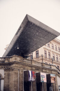 Soravia Wing roof extension of Albertina Museum during snowfall with exhibition banners.