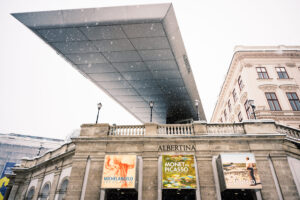 Albertina Museum facade with Soravia Wing canopy and exhibition banners in winter snow.