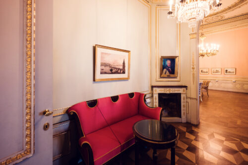 Cozy interior corner of Albertina Museum with a red sofa and classic artwork.