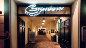 Illuminated Brandauer neon sign above the arched entrance hallway at night.