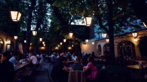 Crowded beer garden with hanging lanterns on a summer evening at Brandauer's Schlossbräu.