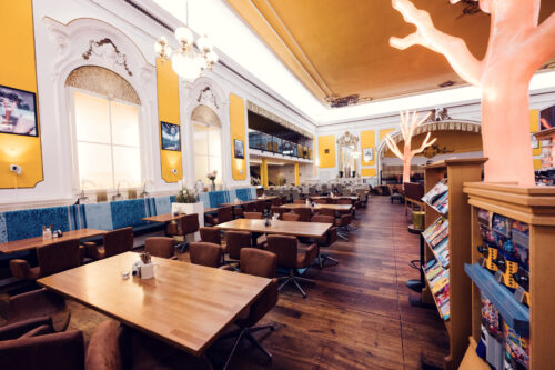 Bright interior with wooden tables and a magazine rack inside Brandauer's Schlossbräu.
