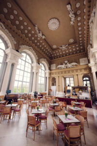 Café Gloriette main hall with decorated ceiling, columns and a grand piano in the corner.