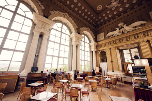 Inside Café Gloriette with high decorated ceilings, arched windows and café tables.