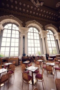 Empty café tables beneath the decorated ceiling and tall arched windows of Café Gloriette.