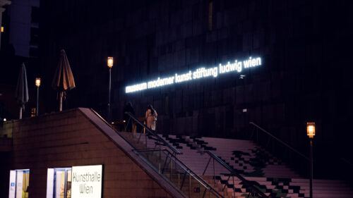 Night perspective of MUMOK Vienna's basalt cube with subtle lighting accentuating the monolithic form in the quieter evening atmosphere of MuseumsQuartier.