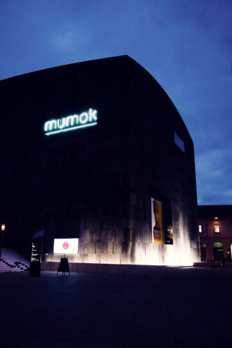 MUMOK Vienna's dark basalt facade at blue hour with the evening sky behind it.