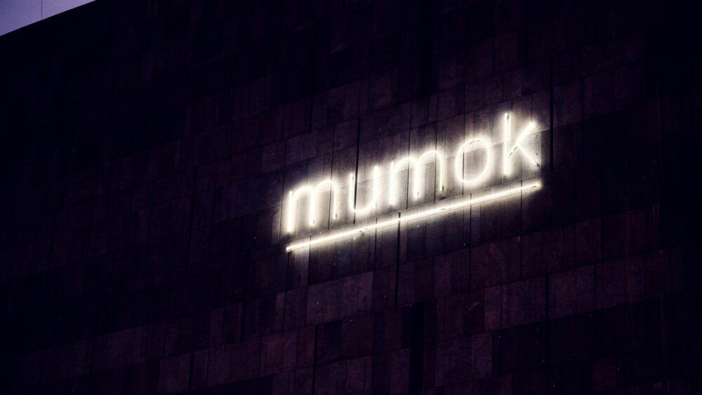 Illuminated MUMOK sign at night on the dark basalt facade of Museum Moderner Kunst Vienna.