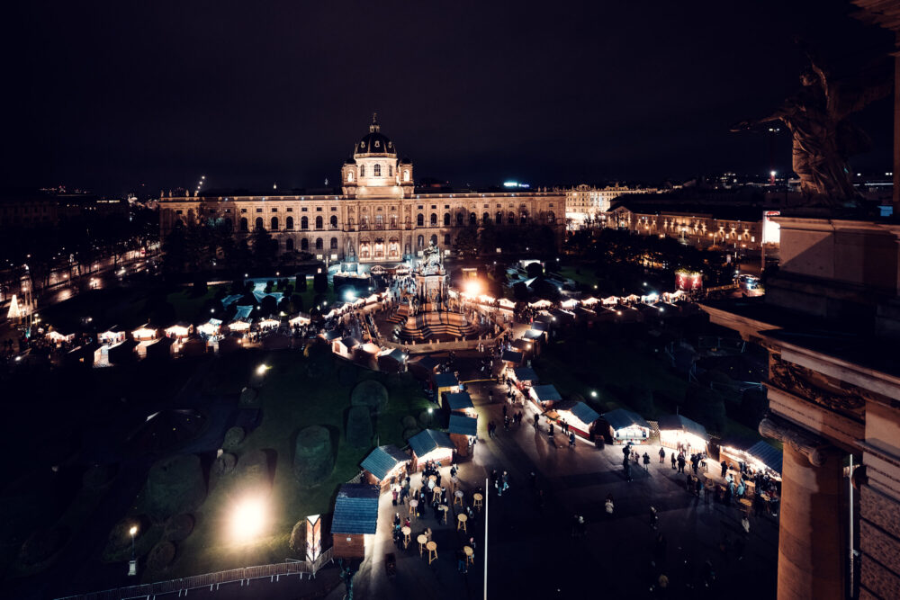 Mercadillo navideño en el Maria-Theresien-Platz con puestos de madera, luces y decoraciones entre los dos museos.