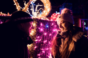 Adriana and Mario standing at a light vendor's stall with handcrafted holiday decorations at the Vienna Rathaus Christmas Market.