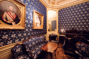 Raum mit blauer Damast-Tapete im Schloss Schönbrunn mit ovalen Porträtgemälden.