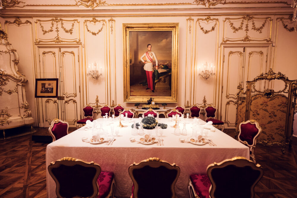 Elegant baroque dining room at Schönbrunn Palace (Schloss Schönbrunn) with red velvet curtains and imperial furniture.