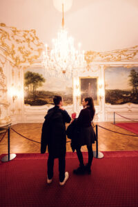 Adriana and Mario viewing artwork at Schönbrunn Palace (Schloss Schönbrunn), baroque imperial palace art collection with historic paintings and ornate golden frames.