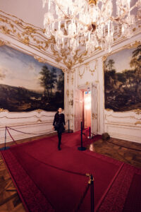Adriana auf rotem Teppich im Schloss Schönbrunn, barockes kaiserliches Palastinterieur mit prunkvollen goldenen Verzierungen und Kristalllüstern.