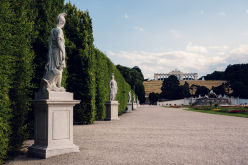 Statua in pietra su un piedistallo lungo un viale alberato nel parco di Schönbrunn.