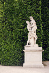 Statua allegorica nei giardini del Palazzo di Schönbrunn con figura in pietra patinata e piedistallo.